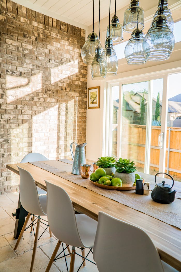 Offerings Sunlit dining room with contemporary decor and a rustic brick wall, featuring stylish lighting and a wooden table.